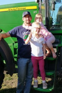 Farmer Brandon Drees and his twin daughters in front of a John Deere tractor
